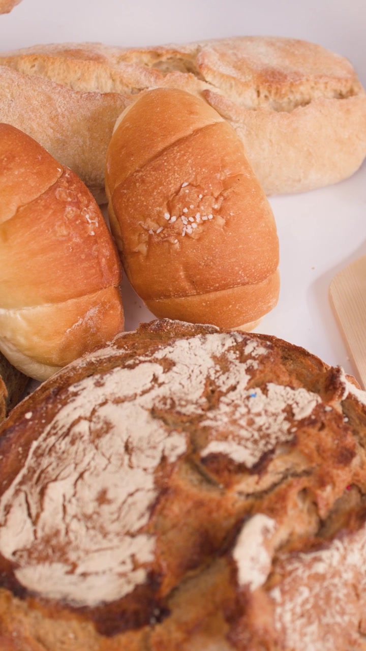 Close-up of hands cutting crusty bread on a wooden board amidst various artisanal loaves.