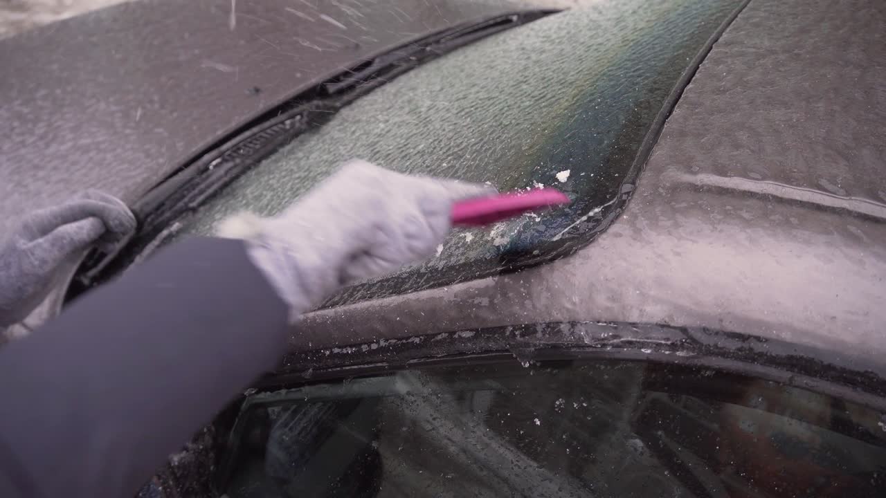 una mujer raspa el hielo del parabrisas de su coche después de un largo estacionamiento.