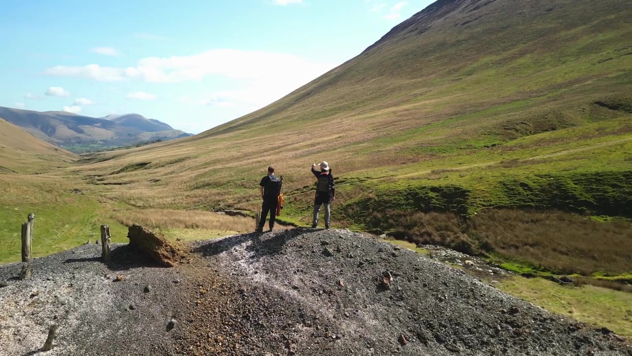 Escursionisti che indicano un cumulo di scorie di una miniera abbandonata a Coledale Beck nel Lake District inglese, Cumbria