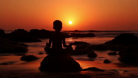 child meditating at sunset on a rocky beach