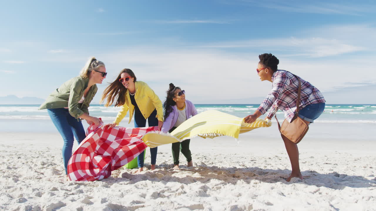 Grupo feliz de amigas diversas divirtiéndose, preparando un picnic en la playa