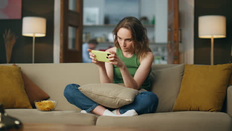 involved gamer playing cellphone sofa room. carefree woman enjoying video games