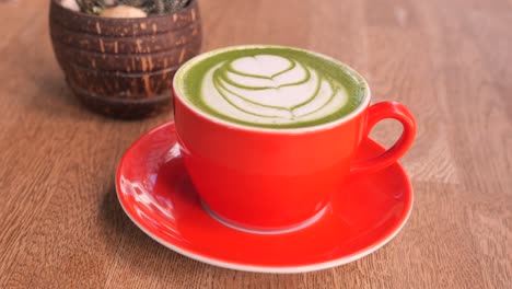 closeup of a matcha latte with latte art in a red cup on a wooden table