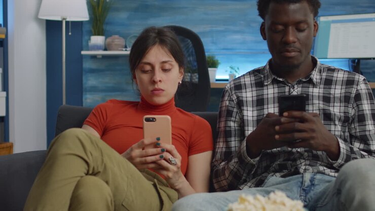 Interracial couple holding smartphones in living room