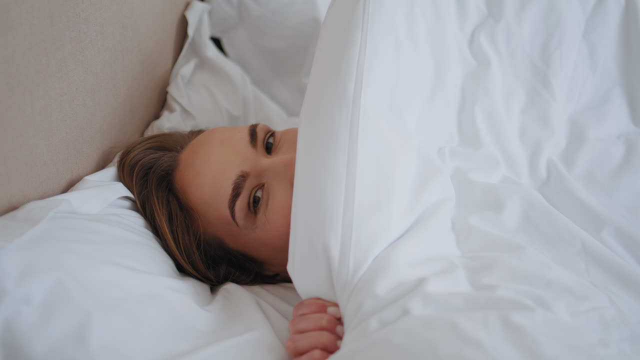 Sleepy woman covering face hiding with blanket closeup. Lazy girl waking up