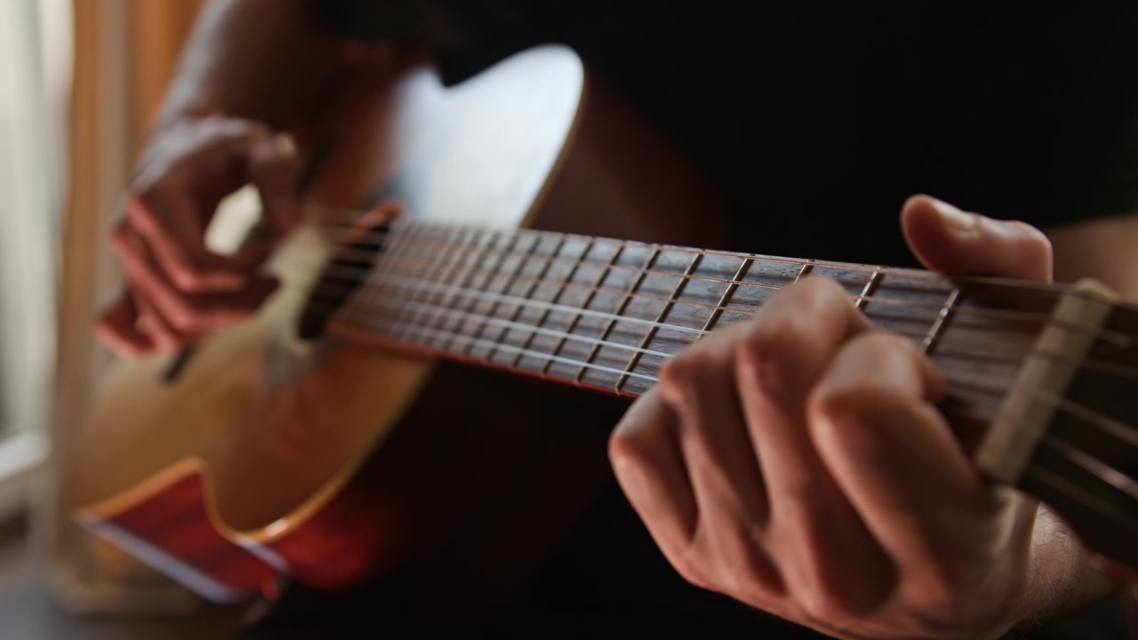 Un primo piano di una persona che suona una chitarra classica acustica al rallentatore, pizzicando gli accordi con le dita. Il video presenta una splendida illuminazione realistica e calda e un'ottima qualità estetica visiva