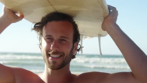 young man carrying surfboard on head at beach