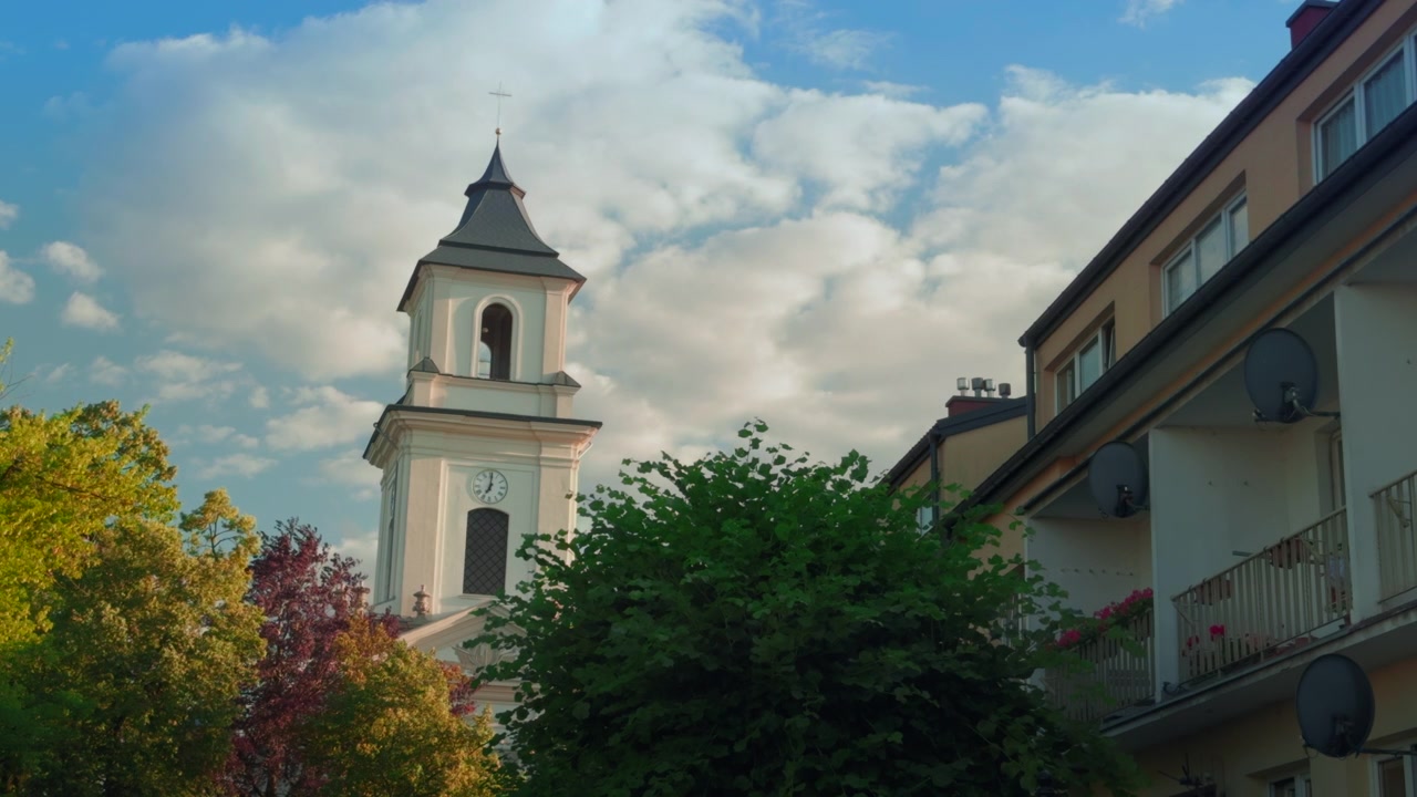 Inquadratura di apertura del campanile storico di una chiesa che si erge sopra alberi ed edifici residenziali in una città dell'Europa orientale - Parrocchia di San Lorenzo a Rymanow, Polonia. Composizione a strati.