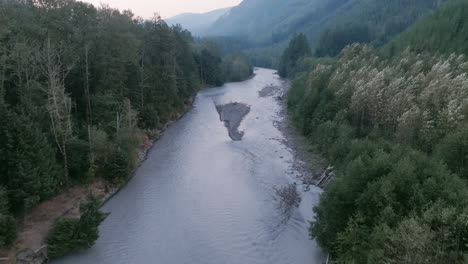 imágenes aéreas volando sobre un río gris entre dos bancos de árboles de hoja perenne en las montañas cascade en washington