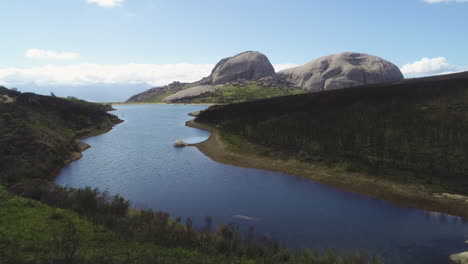 Aerial---Flying-towards-beautiful-dam-on-Paarl-Mountain,-with-imposing-granite-monolith-in-background,-burnt-fynbos-vegetation-visible