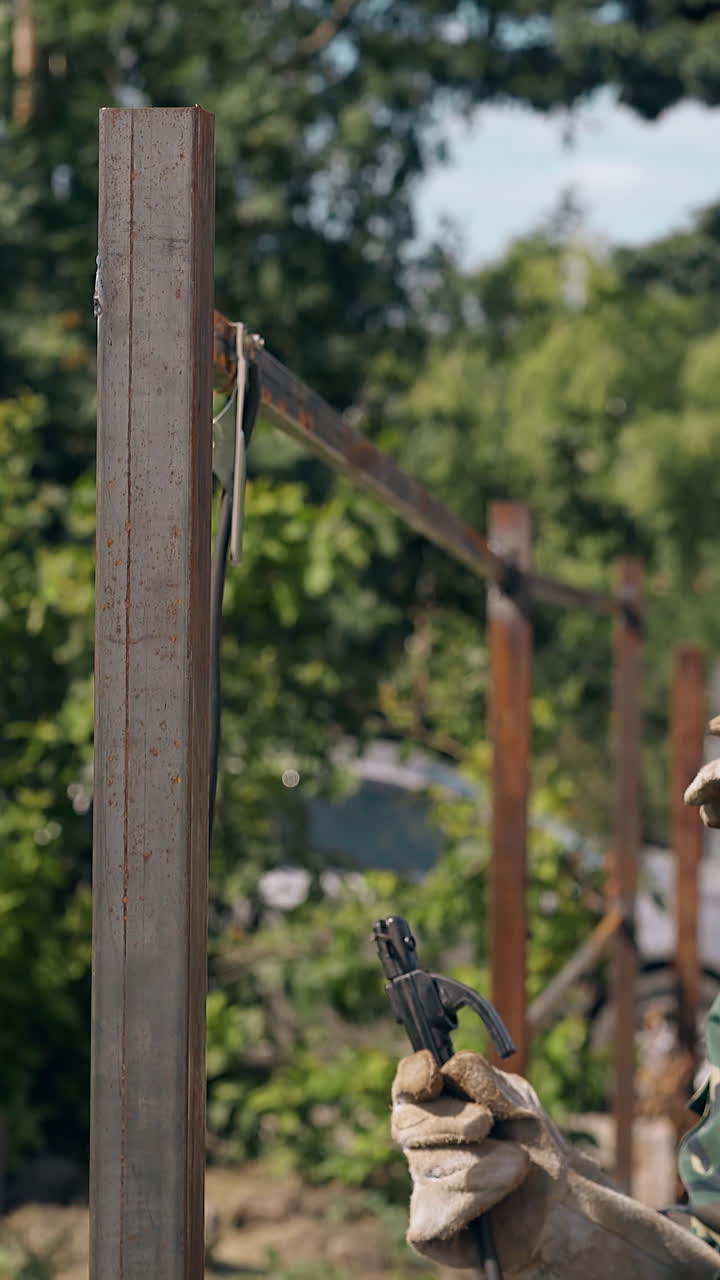 side view professional builder in mask and uniform welds country house fence with new instrument in green yard