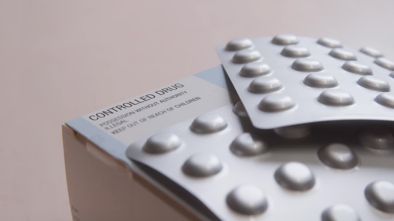 Close up of controlled prescription medication in sealed blister packs placed on pharmaceutical packaging box, sliding left to right. Healthcare, regulation and pharmaceutical industry concept, clip 1