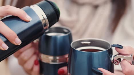 Pouring-a-drink-from-blue-metallic-thermos-to-a-couple-of-mugs-of-the-same-material,-color-and-style