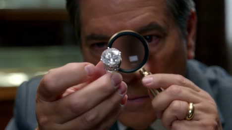 A jeweler examines a diamond ring with a magnifying glass
