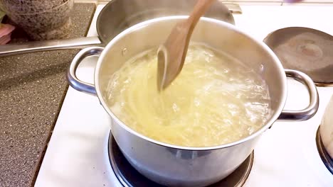 Hand-using-a-wooden-spoon-to-stir-in-a-saucepan-with-spaghetti-in-boiling-water---Cooking-Spaghetti-Bolognese