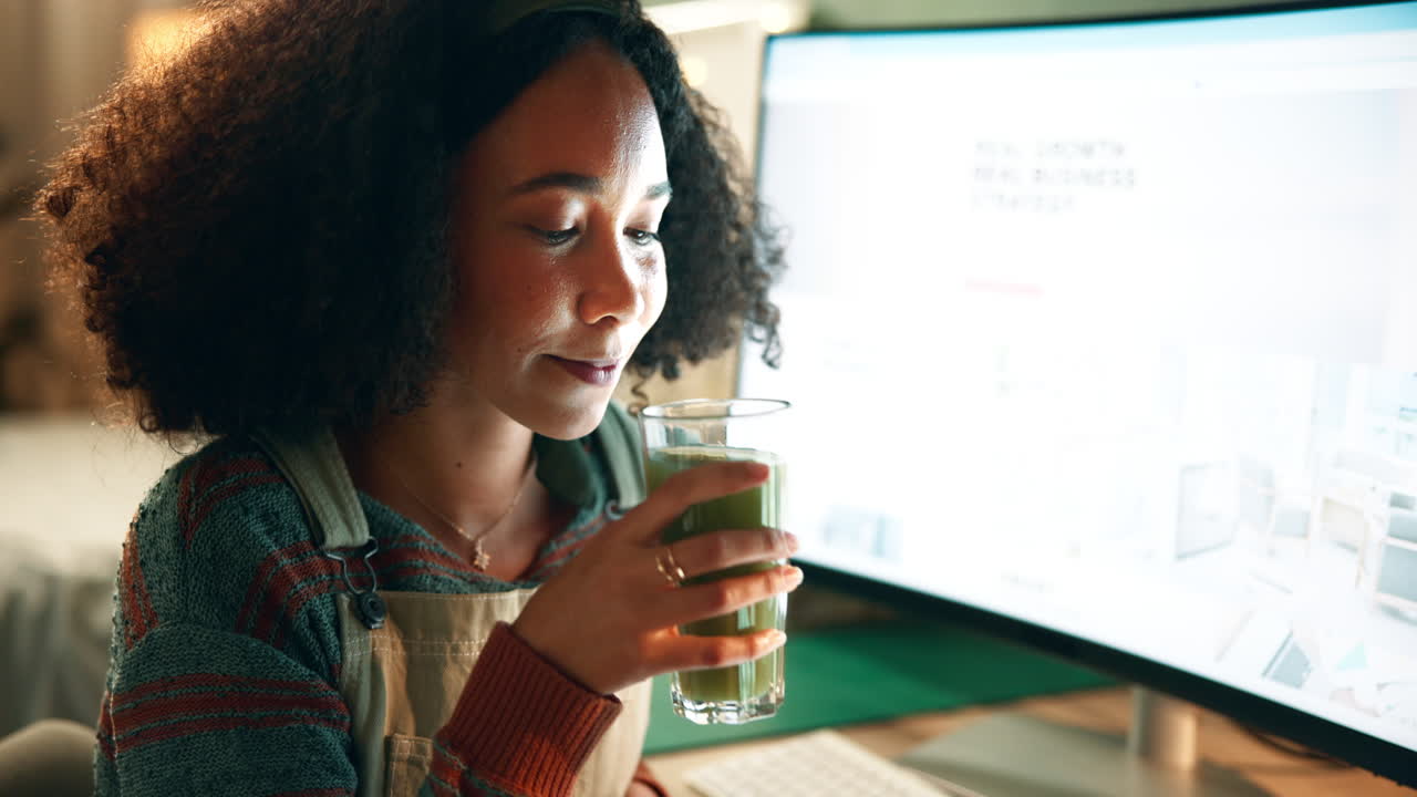 Woman drinking a green smoothie while working at the computer