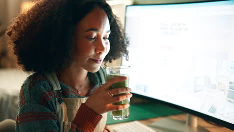 woman drinking a green smoothie while working at the computer