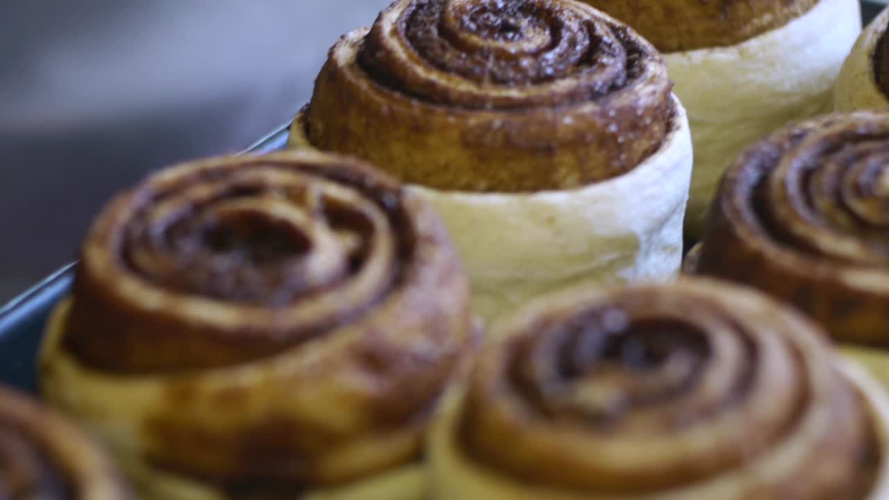 Batch of freshly baked cinnamon rolls pulled out of over and sitting to cool, filmed as extreme close up