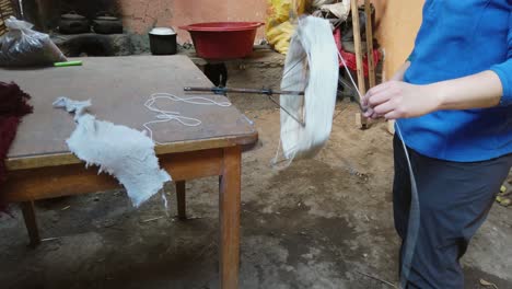 wool swift spinning white yarn beside dyed alpaca wool on a wooden table, inside a traditional workshop near cusco. pan right reveal shot