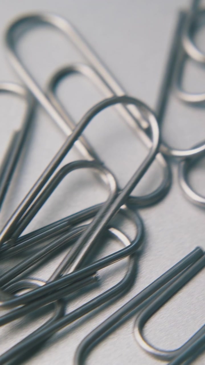 pile of scattered shiny metal paperclips for school and office lies on clean grey background extreme close view