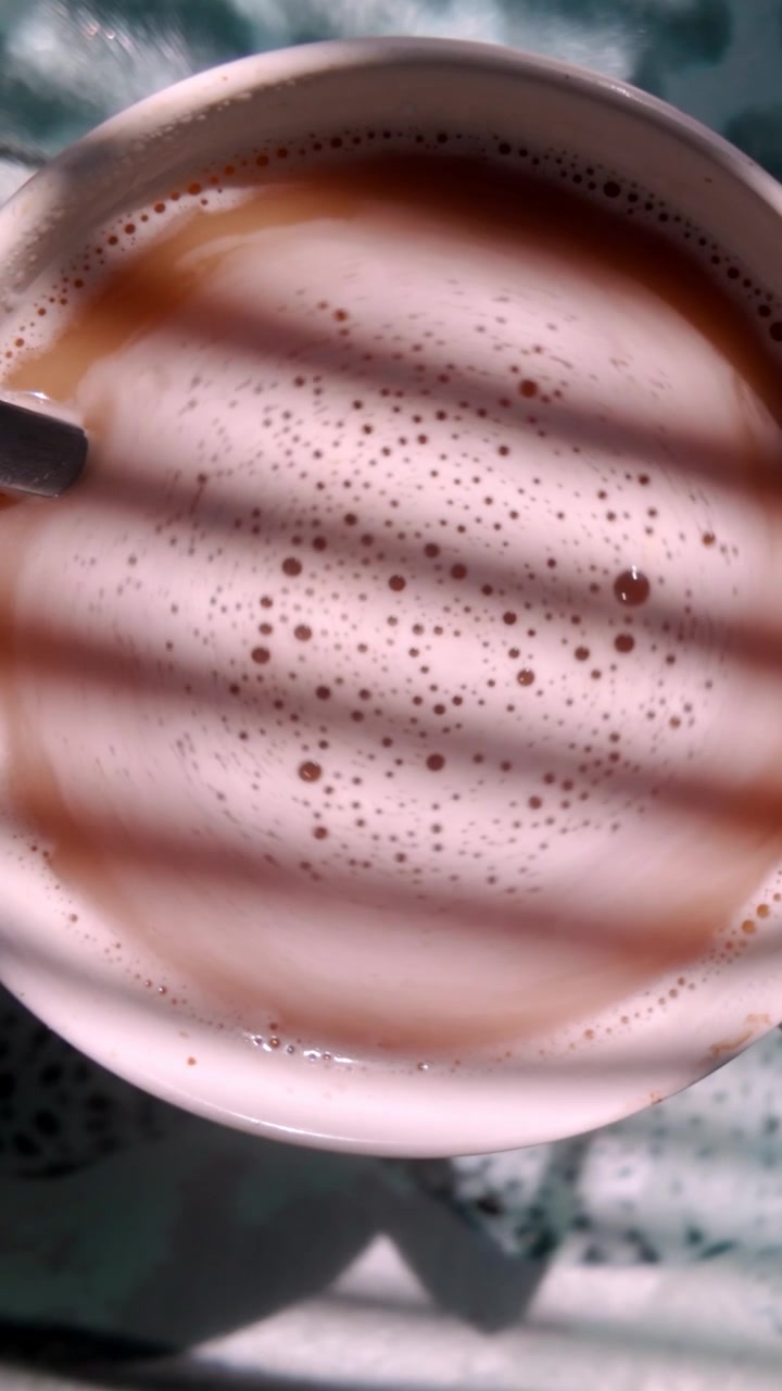 Primo piano verticale estremo di caffè appena mescolato che ruota lentamente sotto la luce solare a motivi. Filmato rilassante ideale per la consapevolezza, i rituali mattutini e la narrazione di lifestyle.