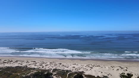 Erleben-Sie-Die-Ruhige-Schönheit-Der-Küste-Mit-Dieser-Atemberaubenden-Aussicht-Auf-Blaue-Meereswellen,-Klaren-Himmel-Und-Sandstranddünen-Im-Vordergrund