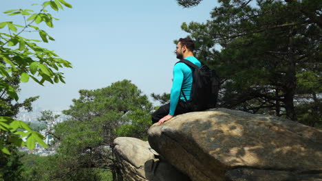 Lone-Hiker-Sitting-on-Mountain-Rock-or-Cliff-Enjoying-Top-View-of-Nearest-City-Skyline-on-Beautiful-Summer-Day---slow-motion-dolly-in