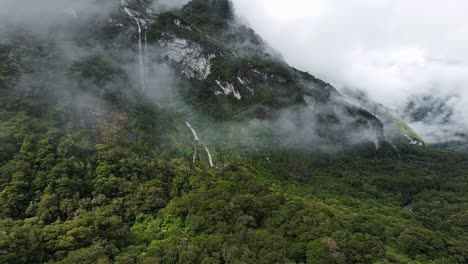 La-Luz-Del-Sol-Brilla-En-El-Denso-Valle-Tropical-Con-Nubes-Envueltas-A-Lo-Largo-De-Una-Alta-Cascada-En-Milford-Sound