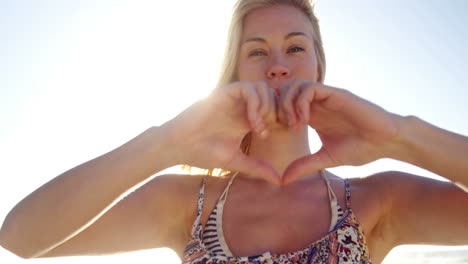 woman making heart shape with hand at beach