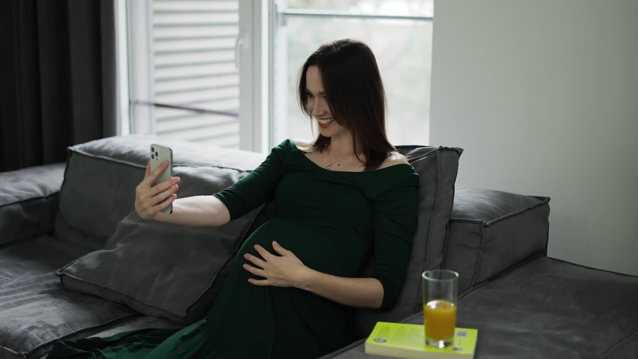 임신 한 여자 가 집 에서 휴대 전화 로 비디오 채팅 하고 있다