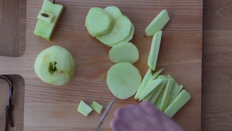 top-down view of a person cutting a peeled apple into small pieces for a meal on a clean wooden table