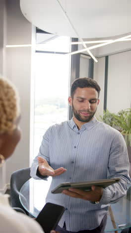 vertical video: discussing project details, man holding tablet and talking to colleague in office