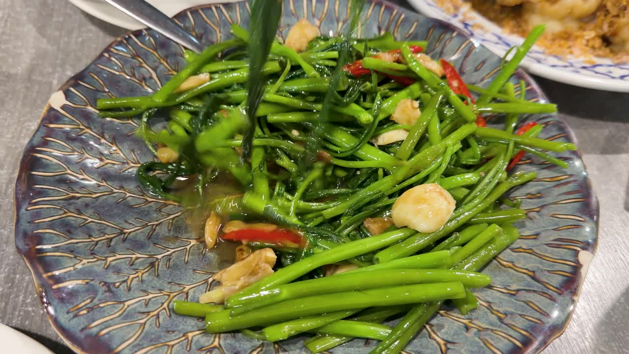 Close-up shot of forks serving Thai stir fried morning glory with garlic and red chili