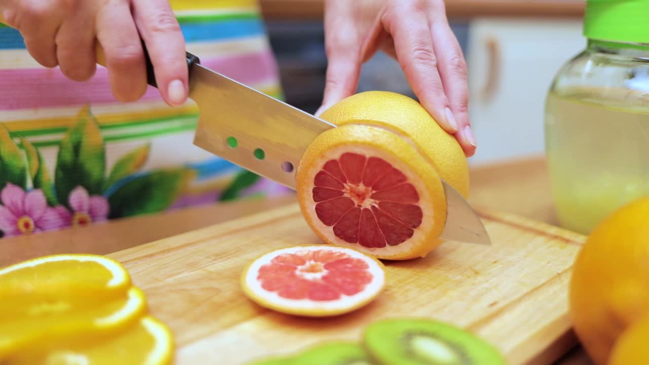 Women's hands Housewives cut with a knife fresh grapefruit on the cutting Board of the kitchen table