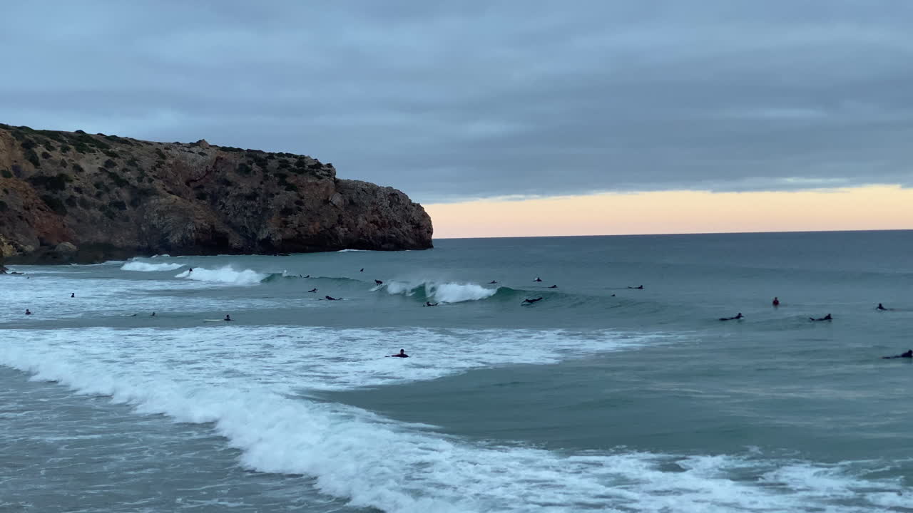 Silhouettes of surfers and friends walking on the beach at dusk, framed by the calm Sagres horizon sunset