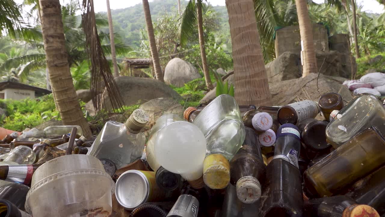botellas de basura recolectadas apiladas bajo palmeras cerca de la playa, toma estable