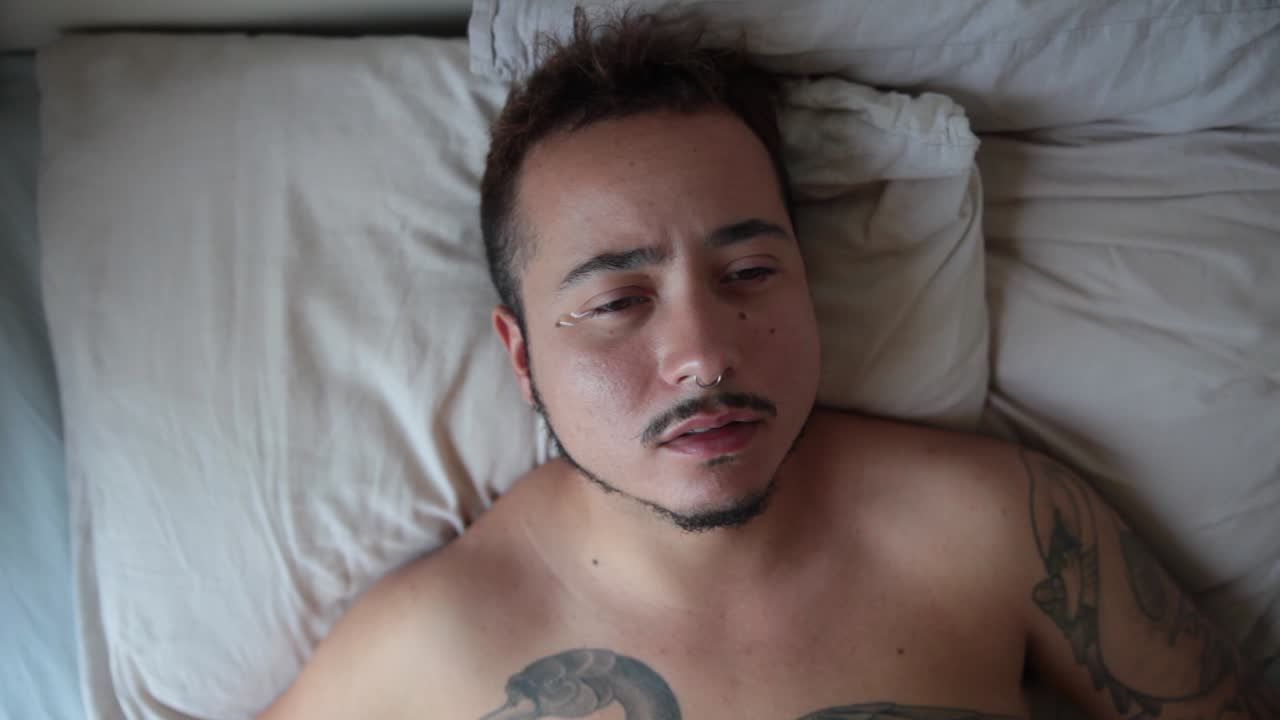 Young Man with Tattoos Crying in Bed
