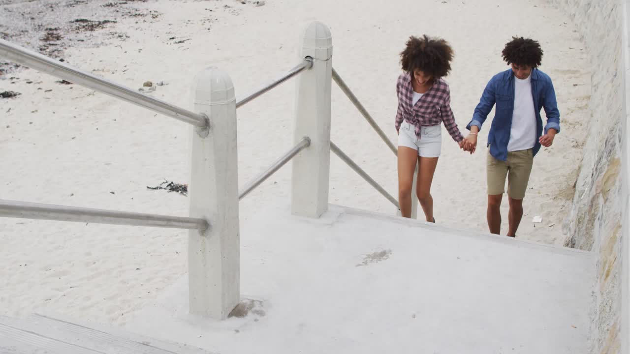 African american couple holding hands climbing up the stairs near the beach