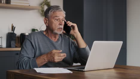 Schockierter-Kaukasischer-älterer-Mann,-Der-Auf-Den-Laptop-Schaut-Und-Telefoniert.