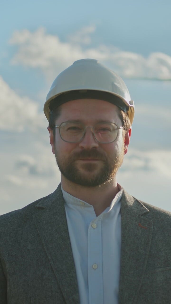 Man in hard hat and suit looks up at cloudy sky contemplating future projects and renewable energy