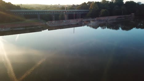 Forward-moving-aerial-over-water-reservoir-towards---ascending-over-railway-bridge