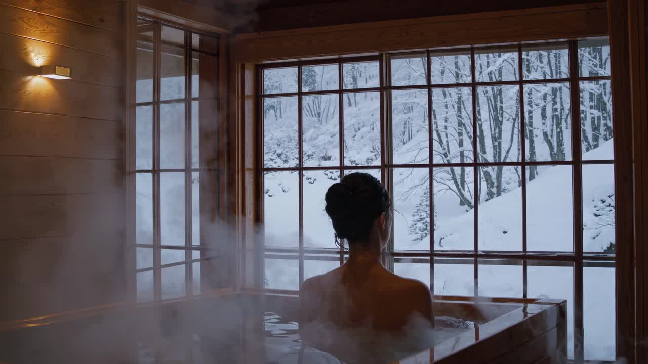 A serene video scene of a woman in a wooden hot tub, viewed from behind