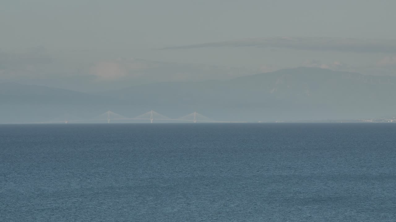 배경에는 산이 있고 전경에는 바다가 있는 먼 다리의 장거리 망원 패닝 샷