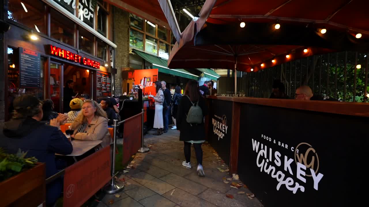 Woman walks through Borough Market in London, surrounded by people and outdoor dining spots