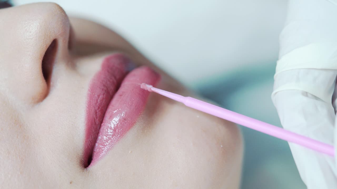 Die Kosmetikerin trägt lokale Betäubung auf die Lippen der Kundin auf. Permanent-Make-up-Behandlung.