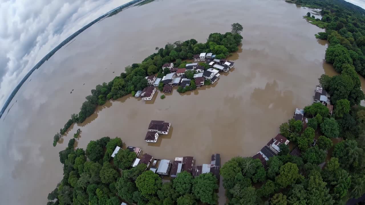 Aerial video captures a flooded village surrounded by water and lush greenery, shot