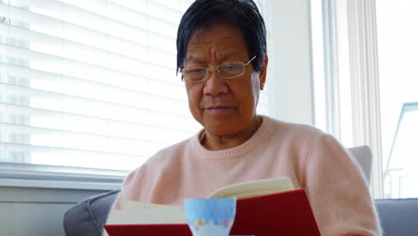 Senior-woman-reading-book-in-living-room