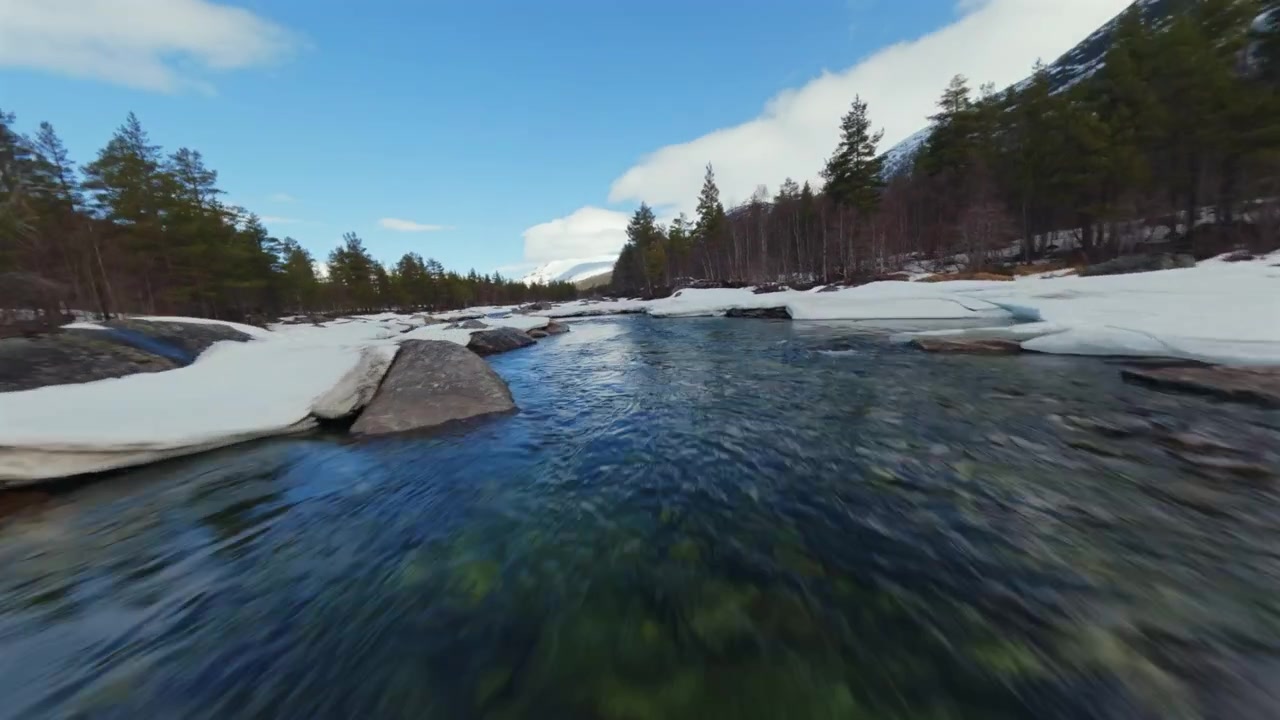 Dron con avance frontal descendiendo por un río a través de un valle boscoso cubierto de nieve en Noruega