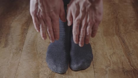 man wearing gray socks standing with feet flat on wooden floor, stretching and reaching toes with both hands