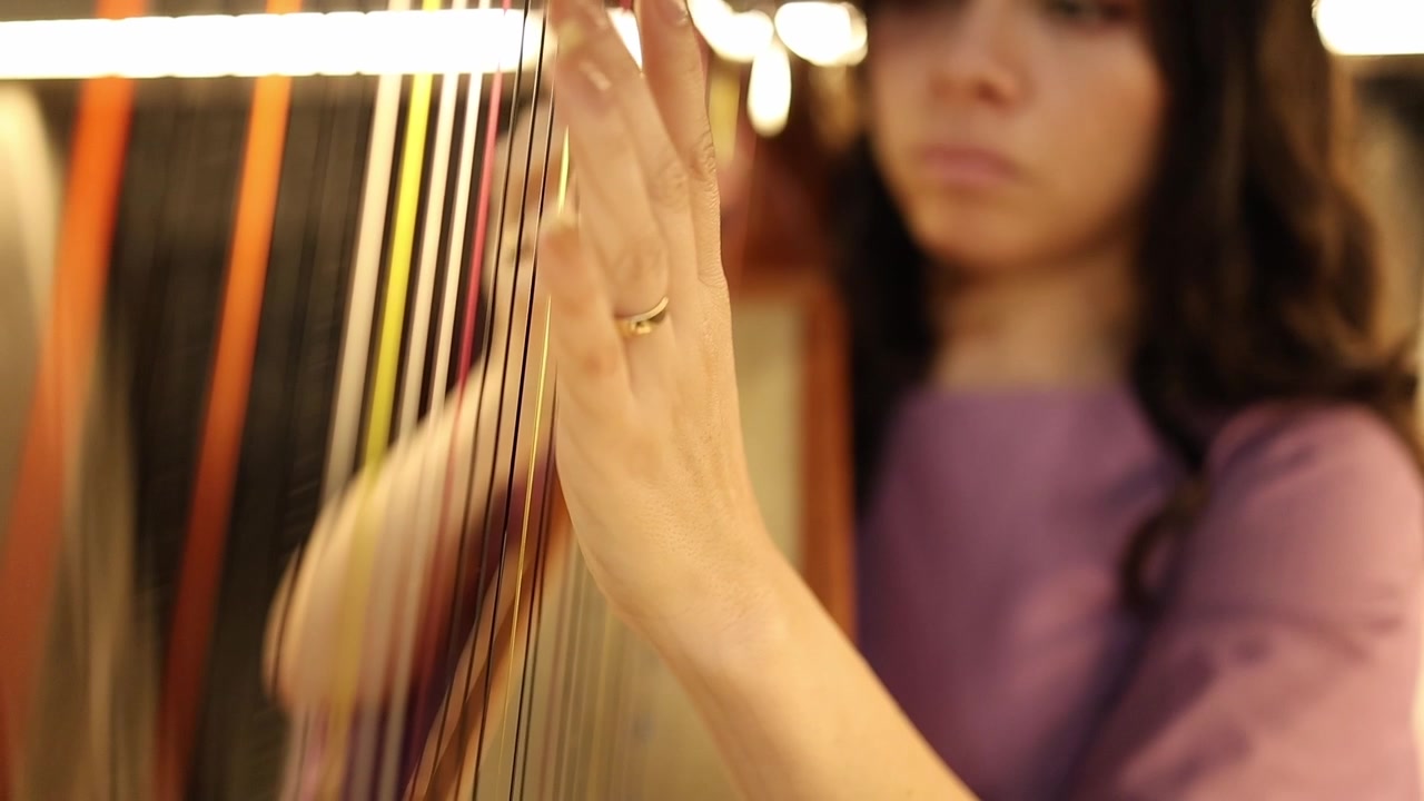 Artistic close-up shot of a woman delicately playing harp strings, her hand in focus with warm bokeh lighting. Captures elegant motion, musical concentration, and vibrant texture detail.
